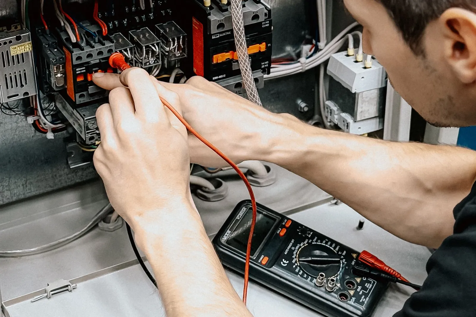 Un electricista prueba conexiones en un panel eléctrico abierto con un multímetro